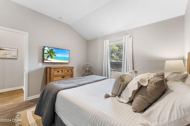 bedroom with vaulted ceiling, wood finished floors, and baseboards