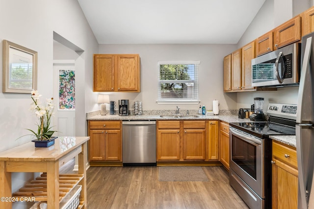 kitchen with light stone counters, a sink, vaulted ceiling, appliances with stainless steel finishes, and light wood finished floors