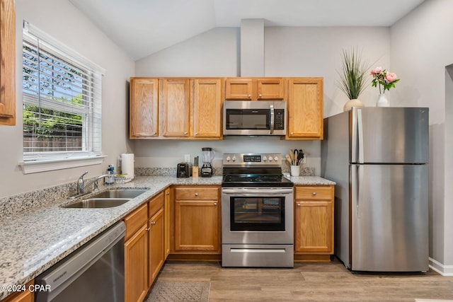 kitchen with light wood-style flooring, a sink, vaulted ceiling, appliances with stainless steel finishes, and light stone countertops