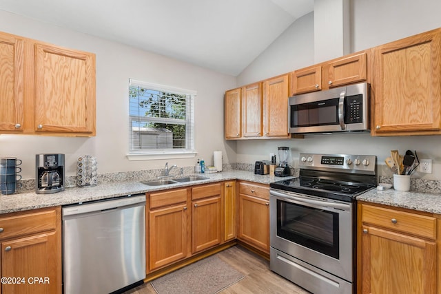 kitchen with light stone counters, light wood-style flooring, stainless steel appliances, a sink, and vaulted ceiling