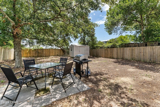 view of patio with an outbuilding, outdoor dining area, a grill, a shed, and a fenced backyard