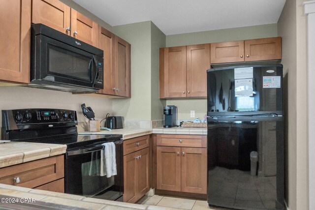 kitchen with tile counters, black appliances, and light tile patterned floors