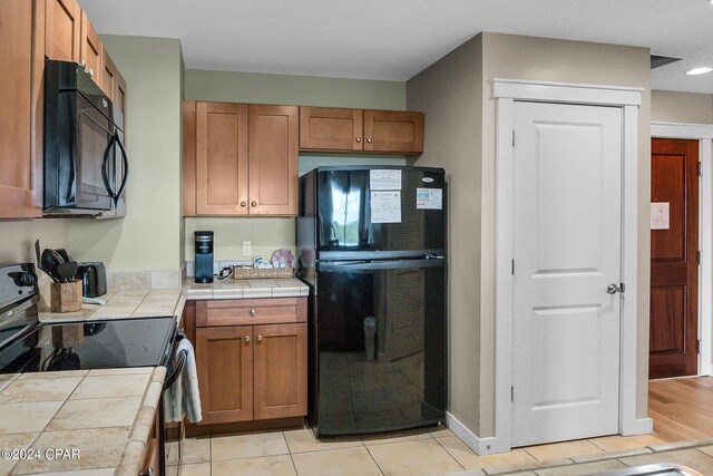 kitchen with tile counters, black appliances, and light hardwood / wood-style flooring