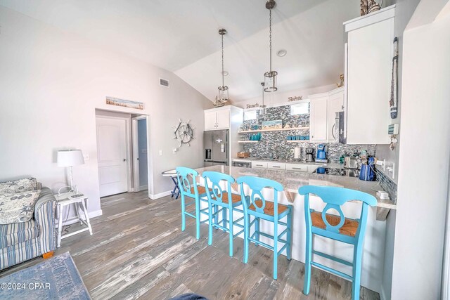 kitchen with stainless steel appliances, white cabinets, decorative backsplash, lofted ceiling, and wood-type flooring