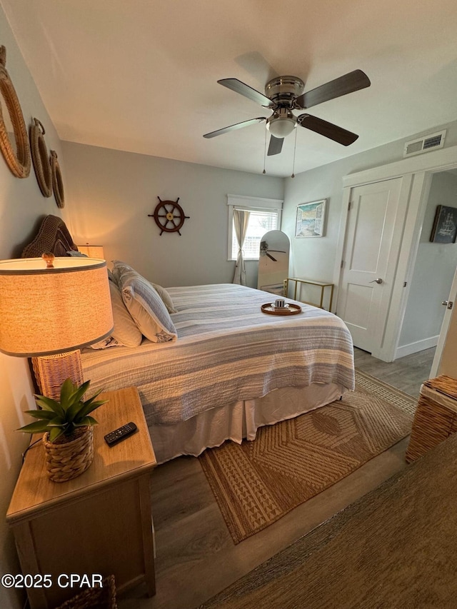 bedroom featuring baseboards, wood finished floors, visible vents, and ceiling fan