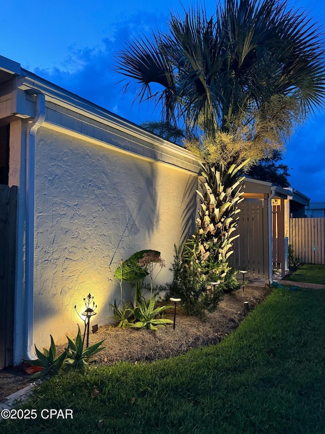 view of side of home with stucco siding, a lawn, and fence