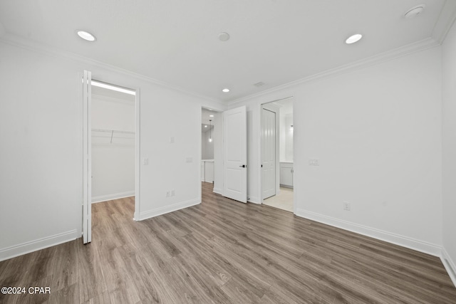 unfurnished bedroom with ornamental molding, a closet, wood-type flooring, and a walk in closet