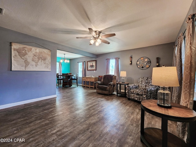 living room with ceiling fan with notable chandelier, dark wood-type flooring, and a textured ceiling