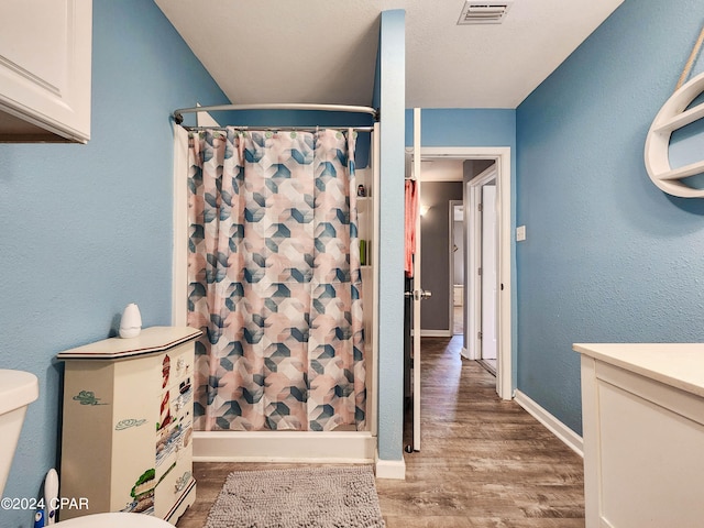 bathroom with toilet, vanity, wood-type flooring, and curtained shower