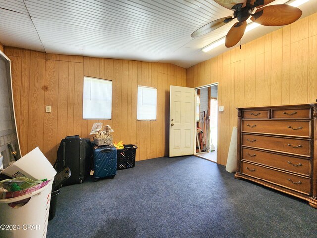 miscellaneous room with wooden walls, ceiling fan, vaulted ceiling, and dark carpet