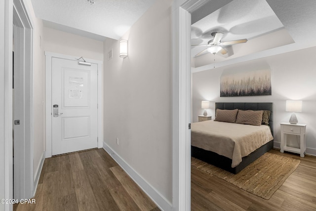 bedroom with ceiling fan, a textured ceiling, hardwood / wood-style flooring, and a raised ceiling