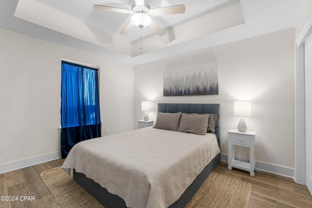 bedroom with ceiling fan, hardwood / wood-style floors, and a tray ceiling