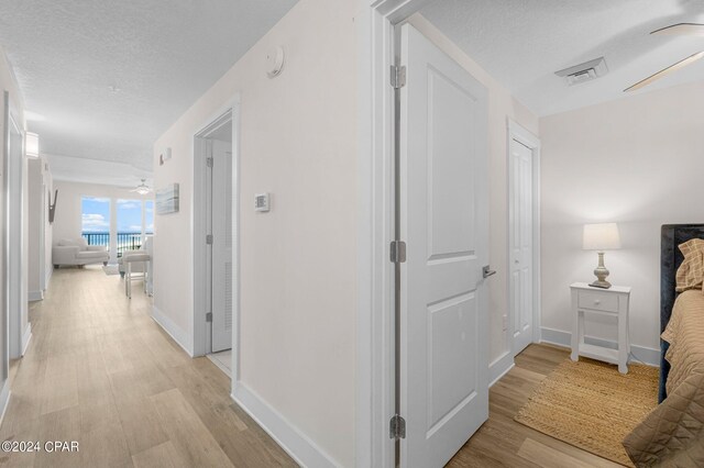 corridor with light hardwood / wood-style floors and a textured ceiling