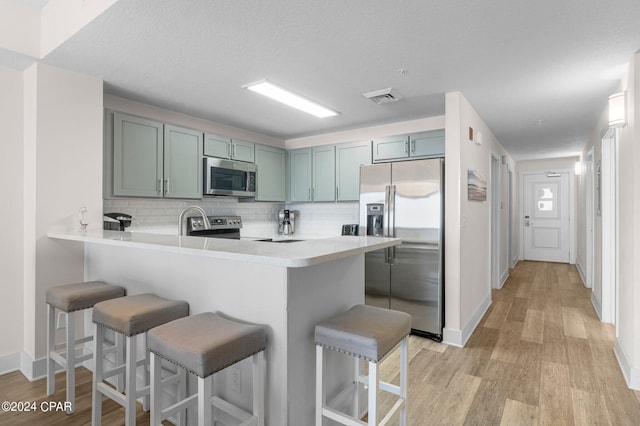 kitchen featuring a kitchen bar, kitchen peninsula, light hardwood / wood-style flooring, and stainless steel appliances