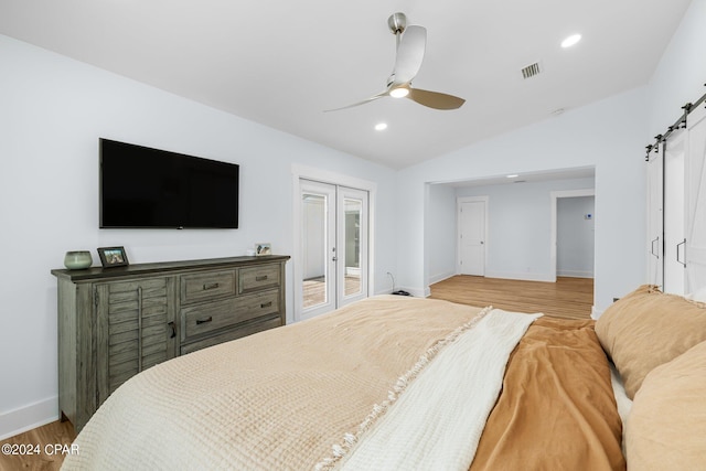 bedroom featuring ceiling fan, a barn door, vaulted ceiling, and light hardwood / wood-style flooring