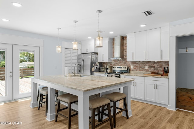 kitchen with white cabinetry, a kitchen island with sink, wall chimney exhaust hood, and appliances with stainless steel finishes