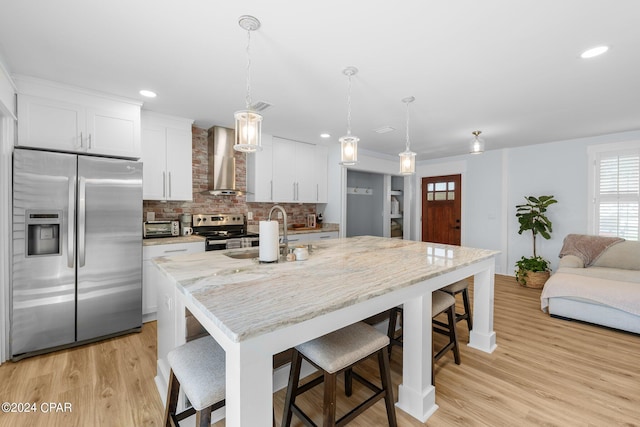 kitchen featuring a kitchen island with sink, white cabinets, stainless steel appliances, and wall chimney exhaust hood