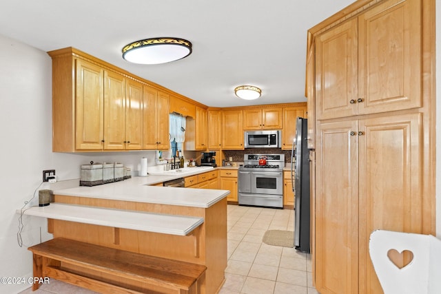 kitchen featuring sink, light tile patterned floors, kitchen peninsula, stainless steel appliances, and backsplash