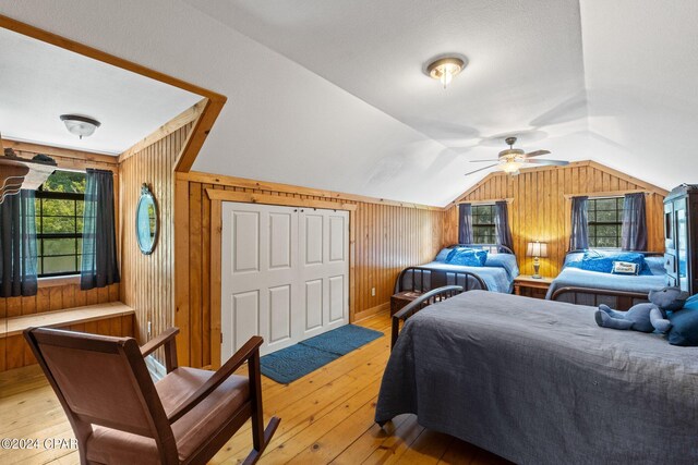 bedroom with lofted ceiling, light wood-type flooring, ceiling fan, and wood walls