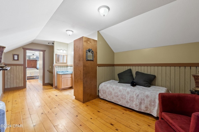 bedroom with ensuite bath, vaulted ceiling, and light hardwood / wood-style floors