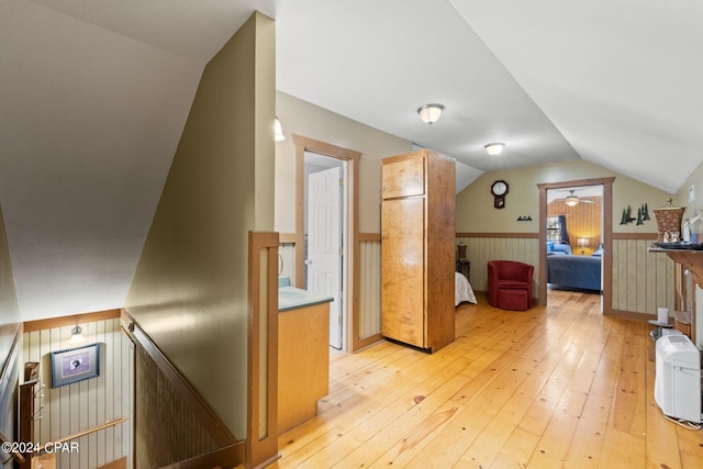 bonus room with vaulted ceiling, wooden walls, and light wood-type flooring