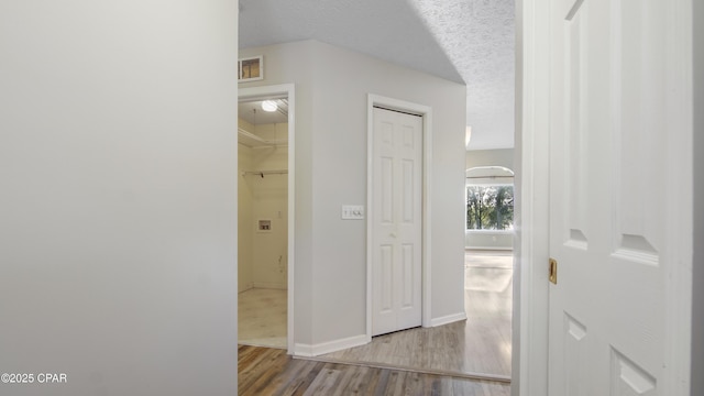 hall with baseboards, a textured ceiling, visible vents, and wood finished floors