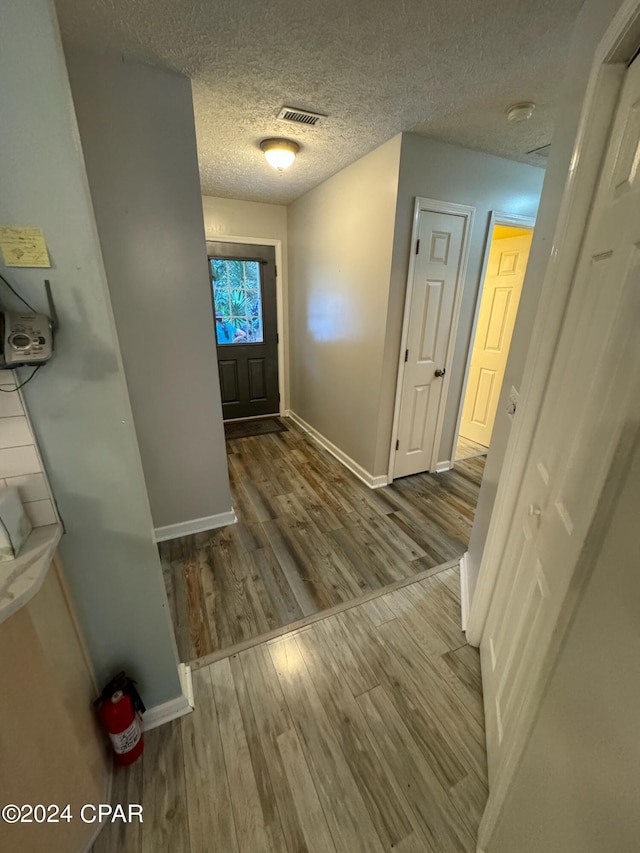 interior space featuring a textured ceiling, wood finished floors, visible vents, and baseboards