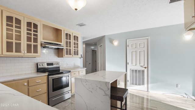 kitchen featuring under cabinet range hood, stainless steel range with electric stovetop, visible vents, a center island, and glass insert cabinets