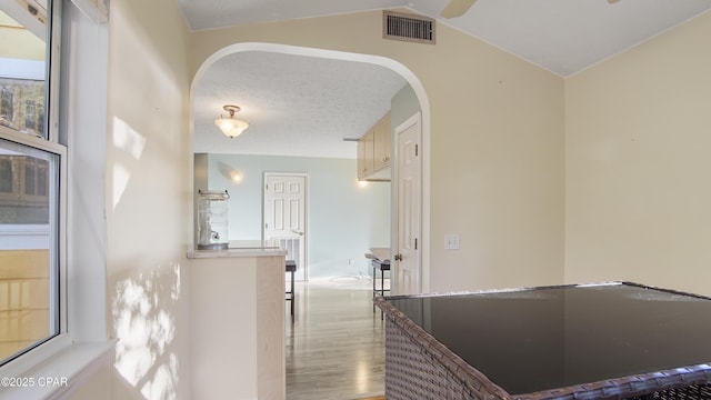 hallway featuring visible vents, arched walkways, lofted ceiling, wood finished floors, and a textured ceiling