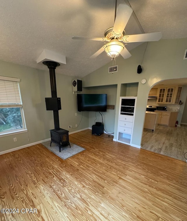 unfurnished living room featuring light wood finished floors, lofted ceiling, a ceiling fan, a wood stove, and a textured ceiling