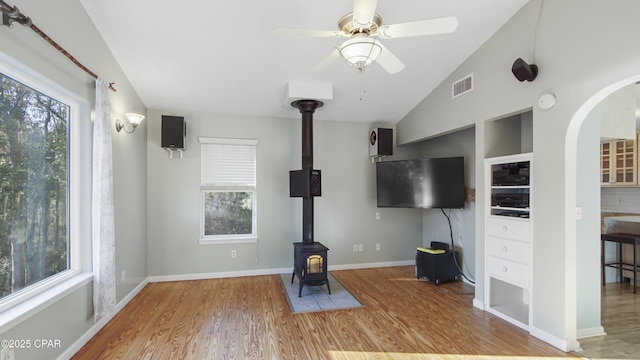 unfurnished living room featuring lofted ceiling, a wood stove, plenty of natural light, and light wood-style flooring