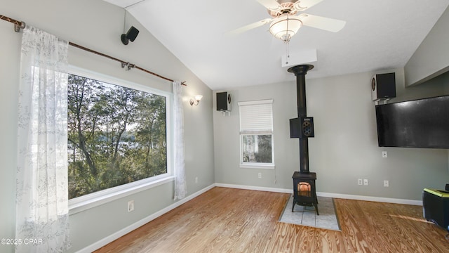 unfurnished living room featuring a wood stove, plenty of natural light, and lofted ceiling