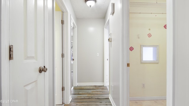 hallway featuring a textured ceiling, wood finished floors, and baseboards