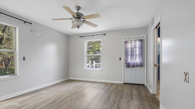 interior space featuring light wood-type flooring, a ceiling fan, baseboards, and a textured ceiling