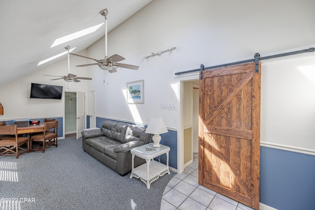 tiled living room with ceiling fan, a skylight, a barn door, and high vaulted ceiling