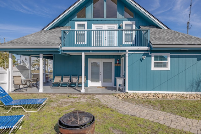 rear view of property featuring french doors, a patio area, a balcony, a lawn, and an outdoor fire pit