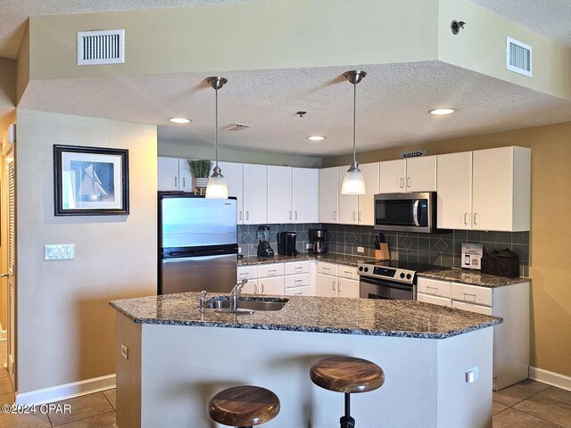 kitchen featuring sink, tasteful backsplash, decorative light fixtures, white cabinets, and appliances with stainless steel finishes