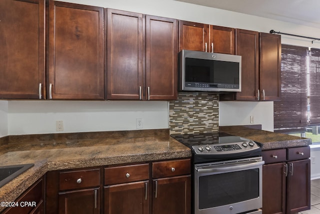 kitchen featuring light tile patterned floors, stainless steel appliances, tasteful backsplash, dark brown cabinetry, and dark stone counters