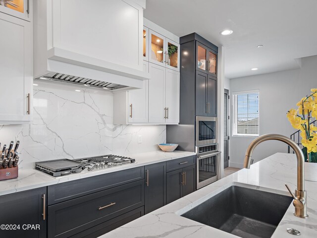 kitchen featuring stainless steel appliances, premium range hood, white cabinetry, and sink