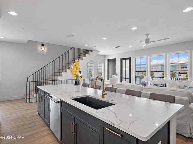 kitchen featuring light stone counters, sink, stainless steel dishwasher, a kitchen island with sink, and light hardwood / wood-style flooring