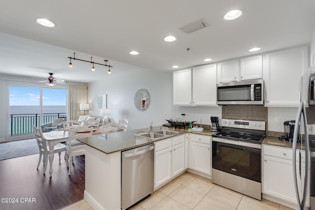 kitchen featuring kitchen peninsula, appliances with stainless steel finishes, sink, a water view, and white cabinetry