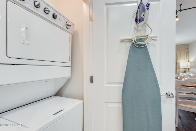 clothes washing area featuring stacked washer / dryer and dark hardwood / wood-style flooring