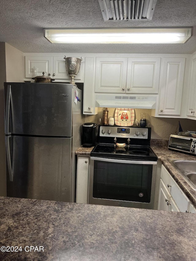 kitchen with a textured ceiling, under cabinet range hood, stainless steel appliances, white cabinetry, and dark countertops