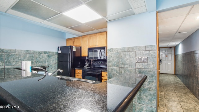 kitchen with tile walls, black appliances, light brown cabinets, and a paneled ceiling