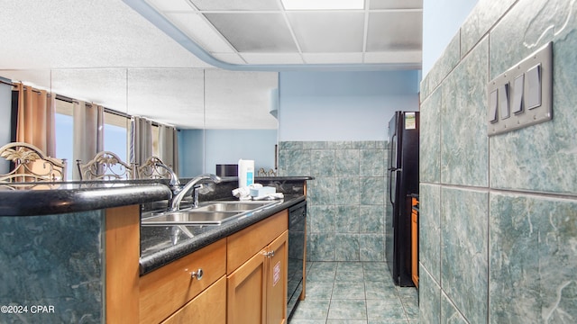 kitchen featuring a drop ceiling, light tile patterned flooring, black appliances, tile walls, and sink