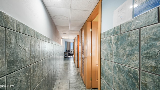 hallway featuring a paneled ceiling, tile patterned flooring, and tile walls