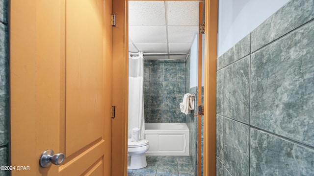 bathroom featuring a drop ceiling, tiled shower / bath combo, toilet, tile walls, and tile patterned floors