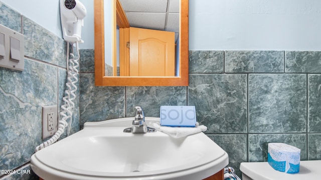 bathroom with tile walls, toilet, sink, and a paneled ceiling