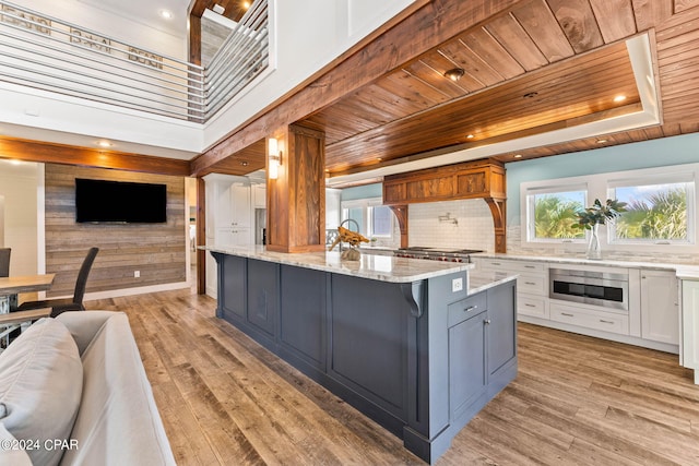 kitchen featuring white cabinets, light wood-type flooring, light stone countertops, and a center island