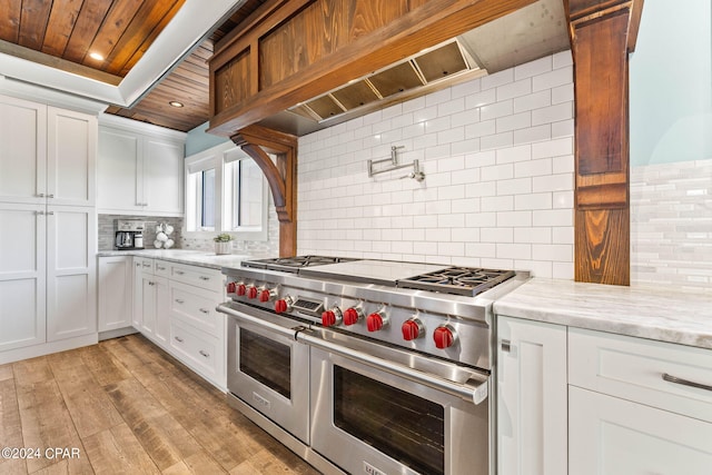 kitchen with light stone counters, white cabinets, backsplash, range with two ovens, and light wood-type flooring